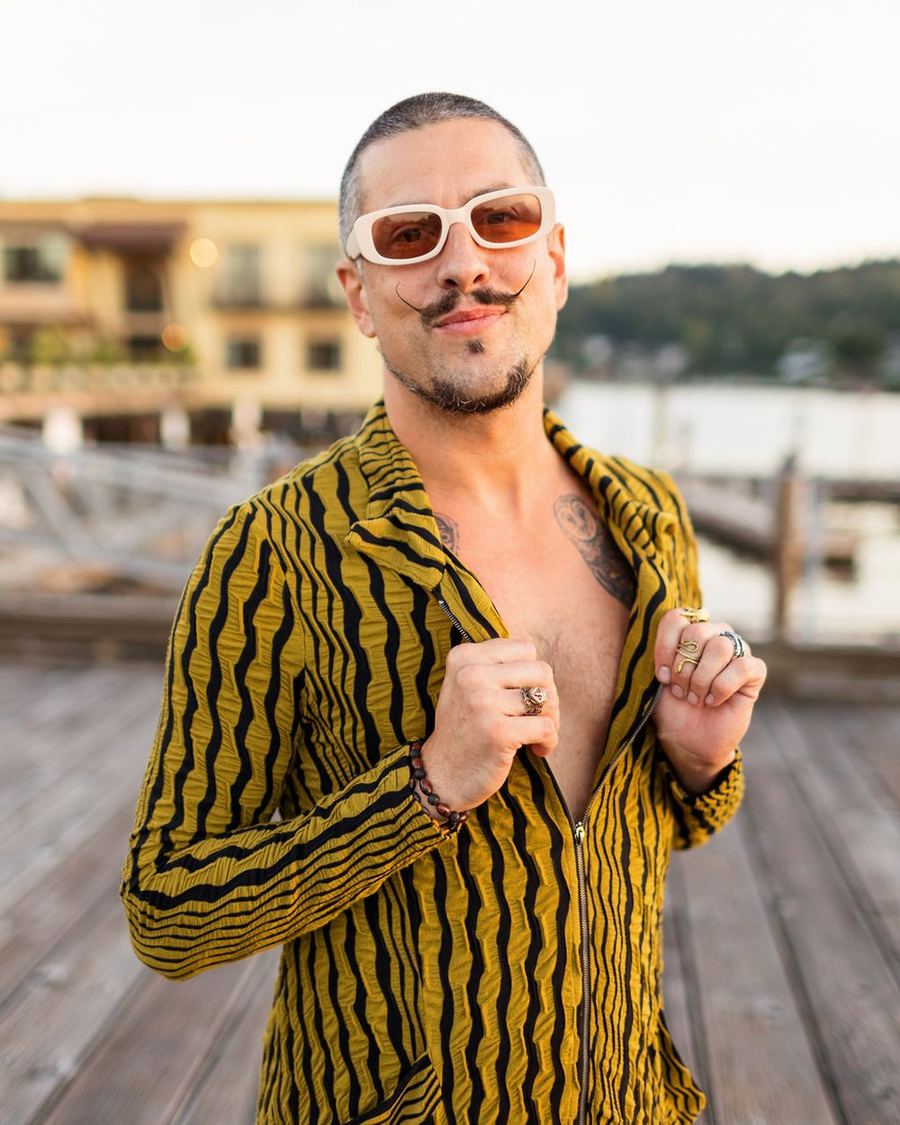 A man in a yellow and black striped jacket and sunglasses on the dock, grinning
