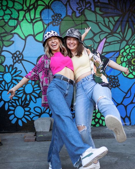 Two friends kicking in front of a flower mural