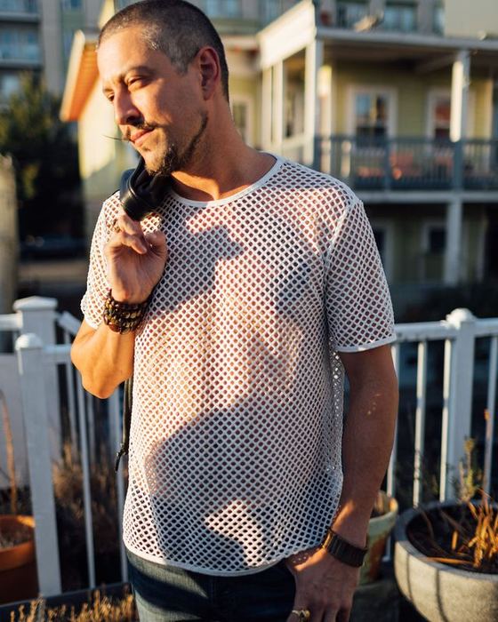 A man in a mesh shirt on a rooftop deck at golden hour