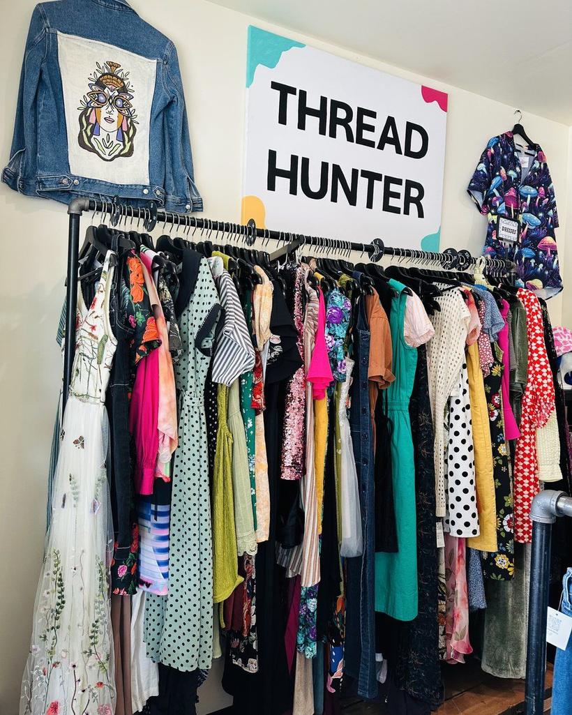 The racks under the Thread Hunter sign: a denim jacket with a patch, dresses, shirts, a mushroom-print robe