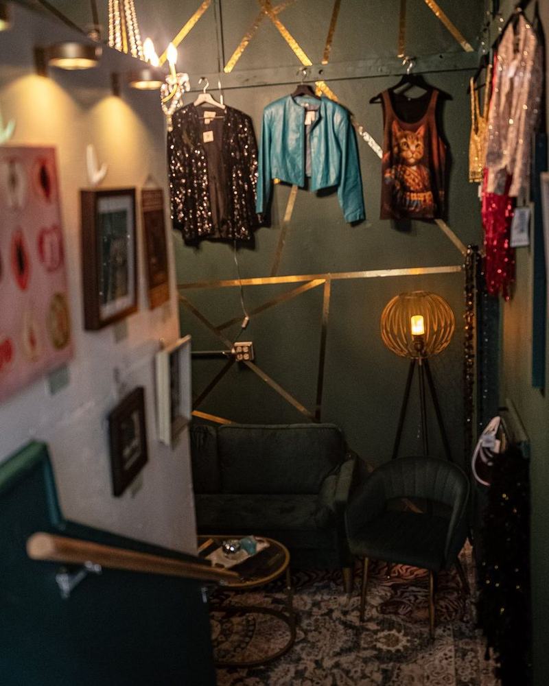 Inside the speakeasy: dark green walls with gold lines, a chandelier, a rack of jackets and a floor lamp